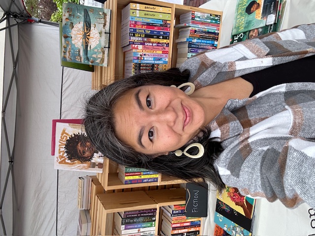 Belonging Books owner, Erica Tso stands in front of an outdoor table full of books.